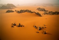 Spitze Sandsteine ragen aus orangenen Dünen im Karnasai-Tal