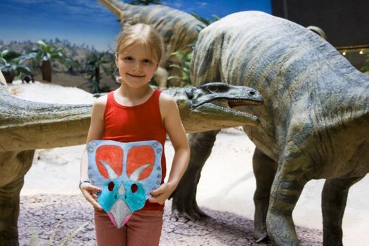 Kind mit bemalter Maske vor Plateosauriern
