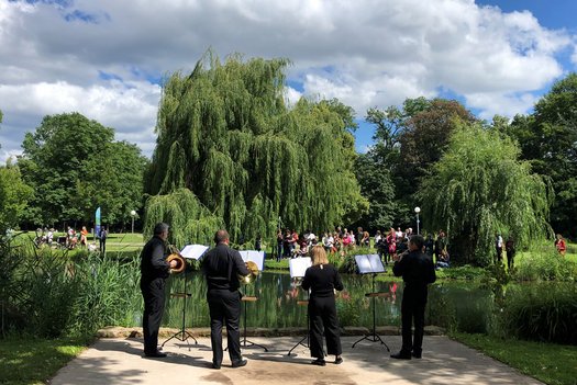Vier Personen musizieren an einem See im Rosensteinpark vor Publikum