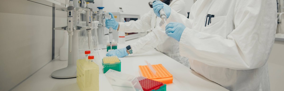 Zwei Personen in Kitteln und Handschuhen arbeiten im Labor und pipettieren