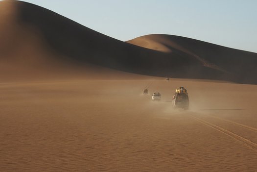 Vier Geländewagen in der Wüste vor Sanddünen.