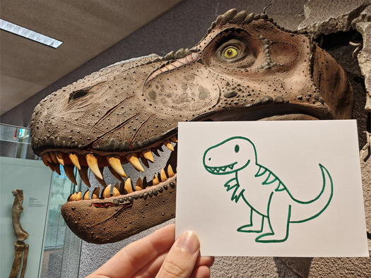 Kinderzeichnung eines Tyrannosaurus wird vor das Kopfmodell eines Tyrannosaurus gehalten