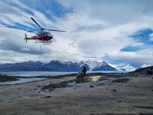 Transporthubschrauber in der Luft über einer Ladung Fossilien vor dem Tyndall-Gletscher