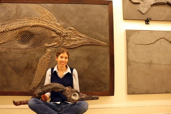 Dr. Erin Maxwell sitzt vor einem Fischsaurierfossil und hält ein Fischsaurierfossil.