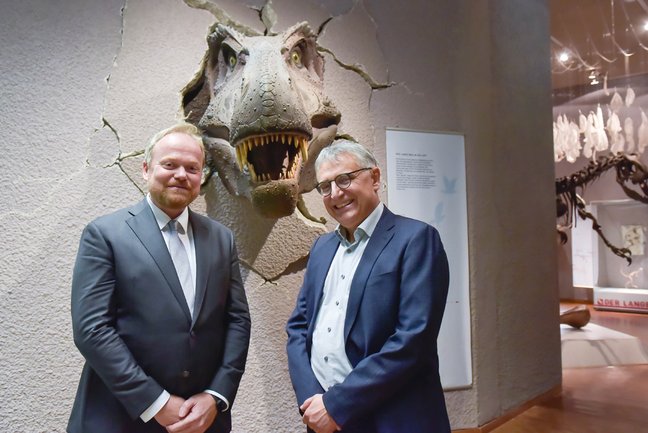 Museumsdirektor Lars Krogmann und Staatssekretär Arne Braun stehen vor dem Modell eines Kopfes von Tyrannosaurus rex.